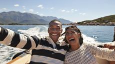 A couple smile and laugh on a boat while he takes a selfie of them.