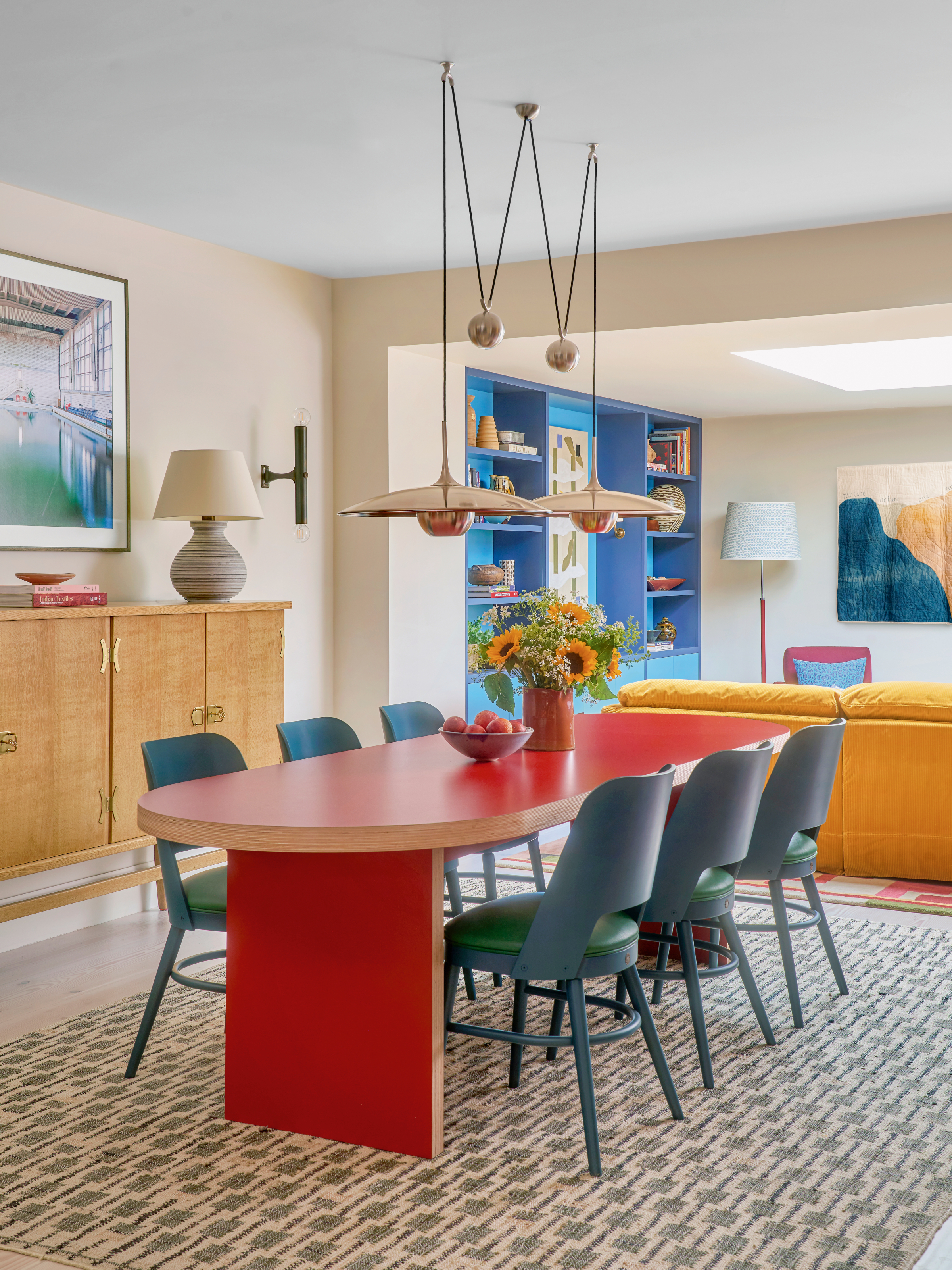 Dining area with red oval table, blue chairs, overhead pendants and a rattan sideboard