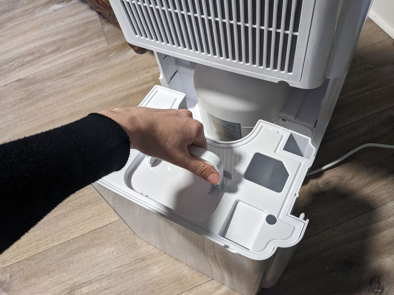 A woman removing the back of a dehumidifier to empty it of water