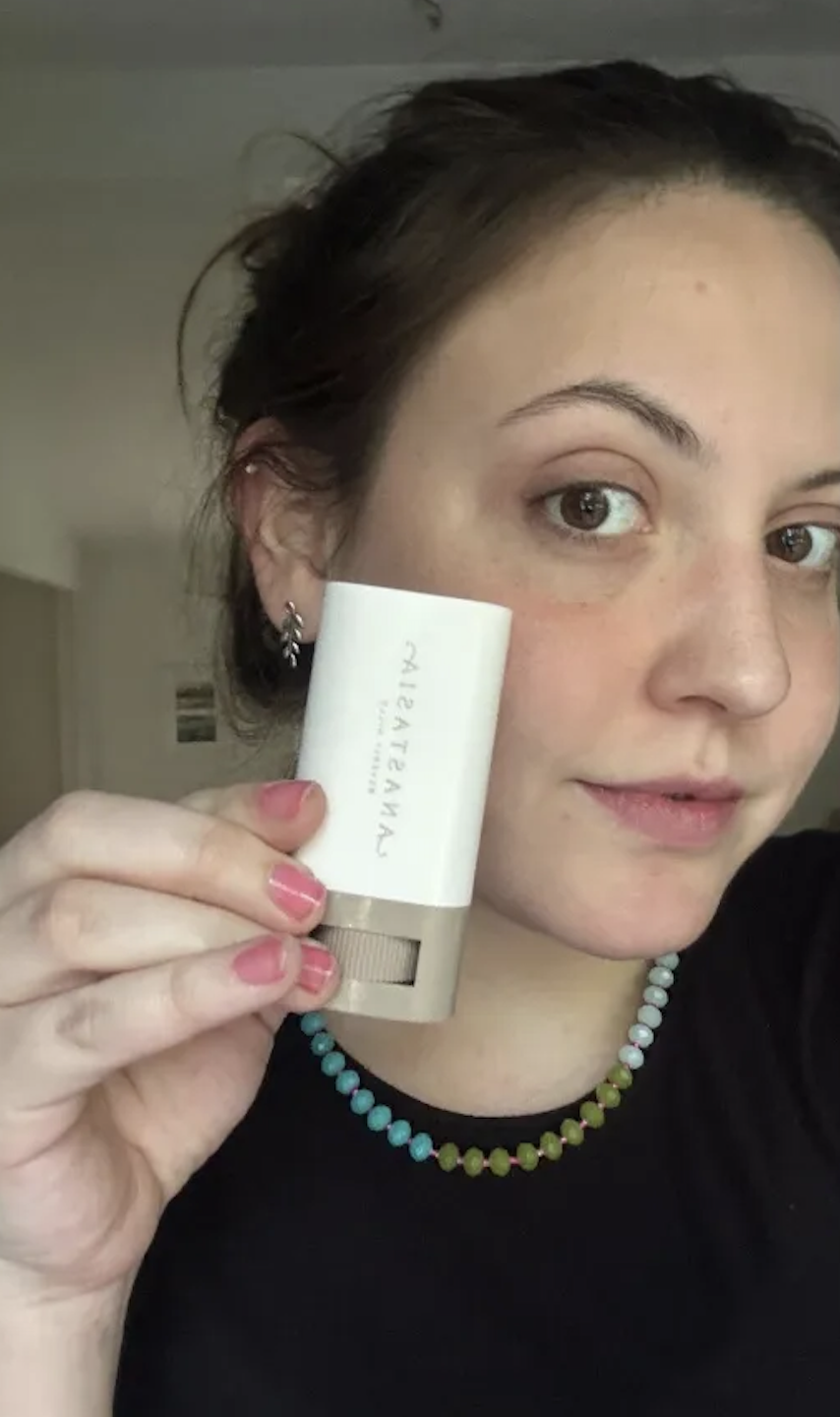 a girl with a black tshirt and clear skin holding the Anastasia Beverly Hills Beauty Balm Serum Boosted Skin Tint.