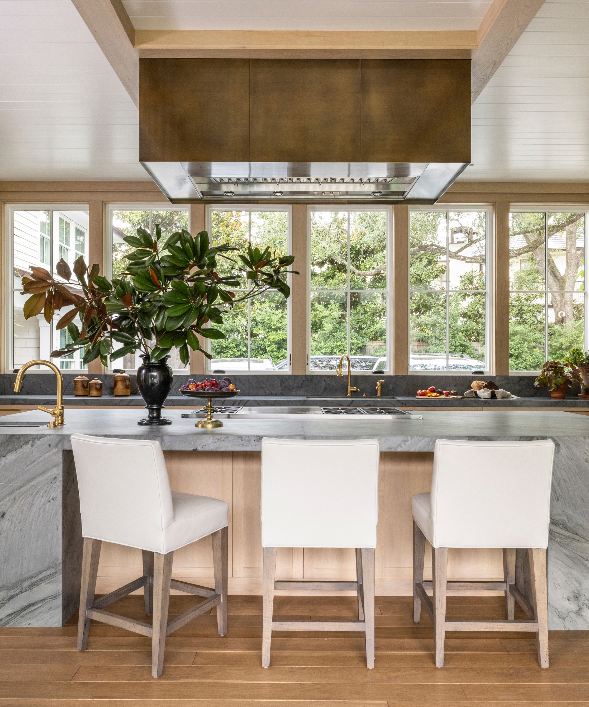 A dramatic kitchen with a large run of windows replacing a standard backsplash. A large marble island frames the center of the kitchen