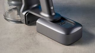 a modern-looking sleek shiny vacuum cleaner with light grey components on a carpet in front of a blue background