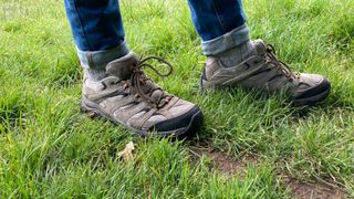 A person wearing Merrell Moab 3 walking shoes standing on wet grass.