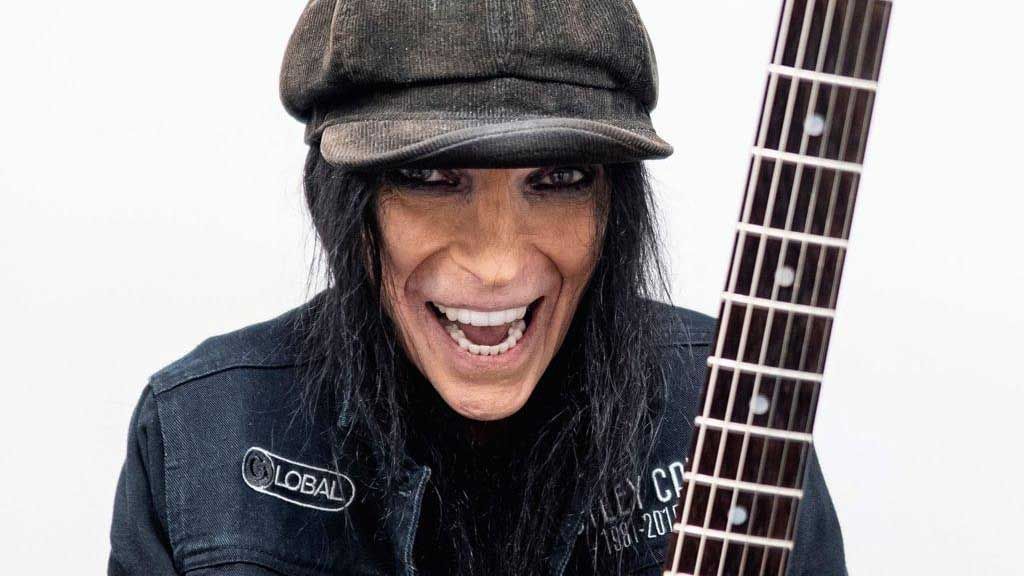 Mick Mars studio portrait. He&#039;s wearing a cap and smiling