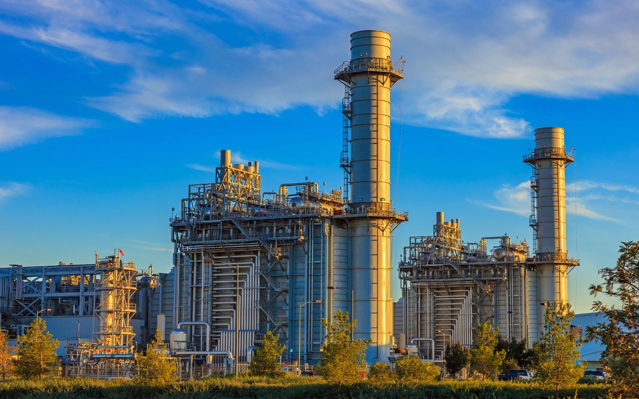 Natural gas fired turbine power plant with it&amp;#039;s cooling towers rising into a cloud filled blue sky