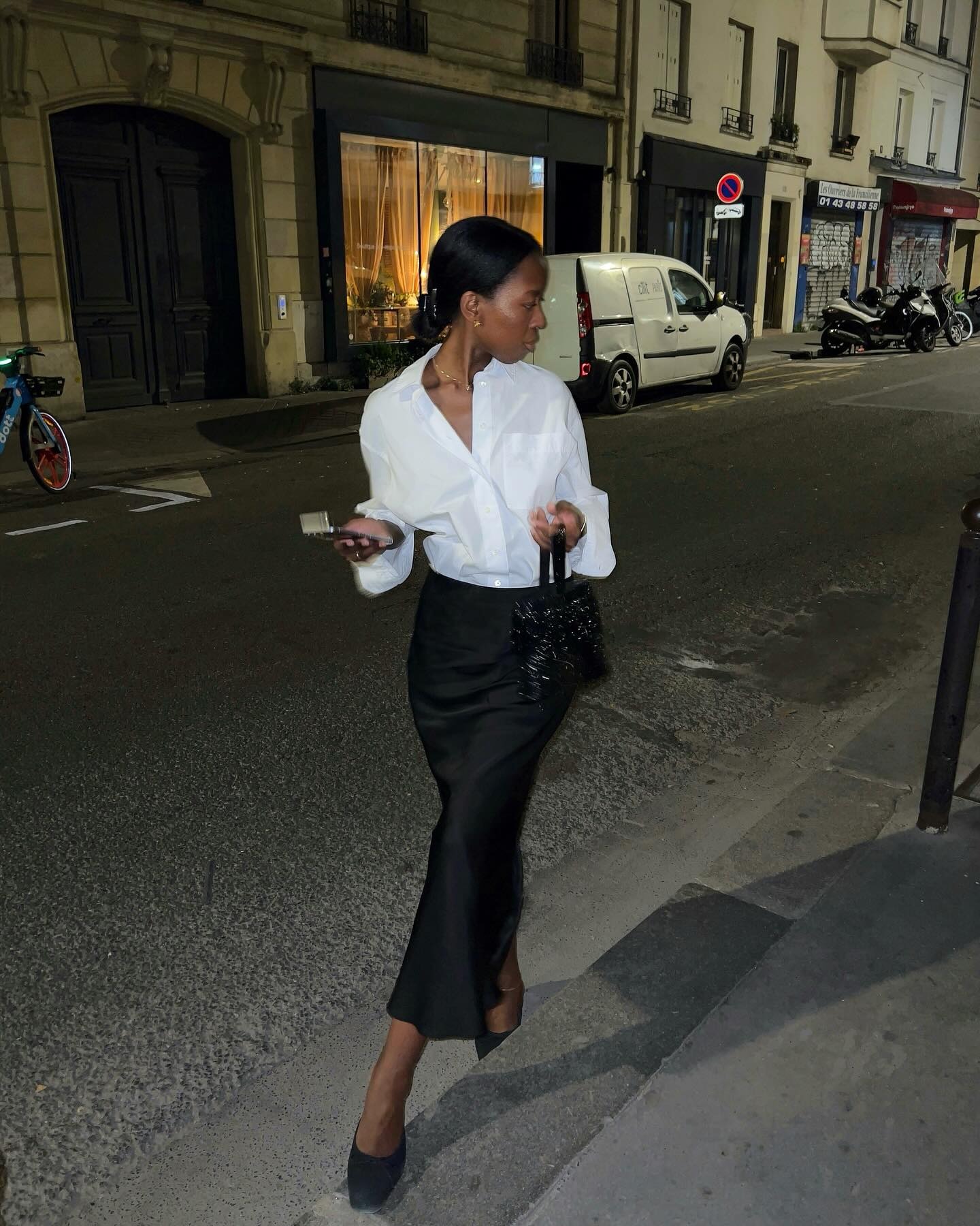 @sylviemus_ wearing a white button-down shirt, black pencil skirt, and black heels.
