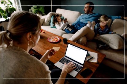 woman looking at laptop while holding credit card while children play on sofa in the background