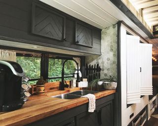 kitchen interior of Caleb's converted bus, with wooden worktops, coffee machine, black tap, and white cupboards beyond