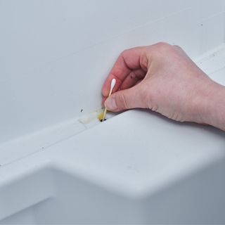 Person using an earbud to unblock the drainage hole in their fridge