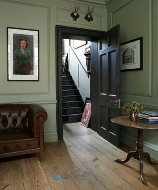 Green panelled living room with wooden flooring and leather Chesterfield sofa