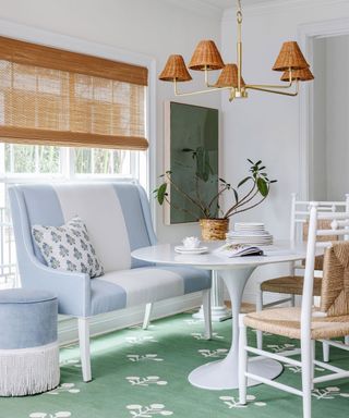 Bright white dining room with white round dining table, white and wood chairs, blue and white sofa, green artwork and rug, wicker style pendant and blind