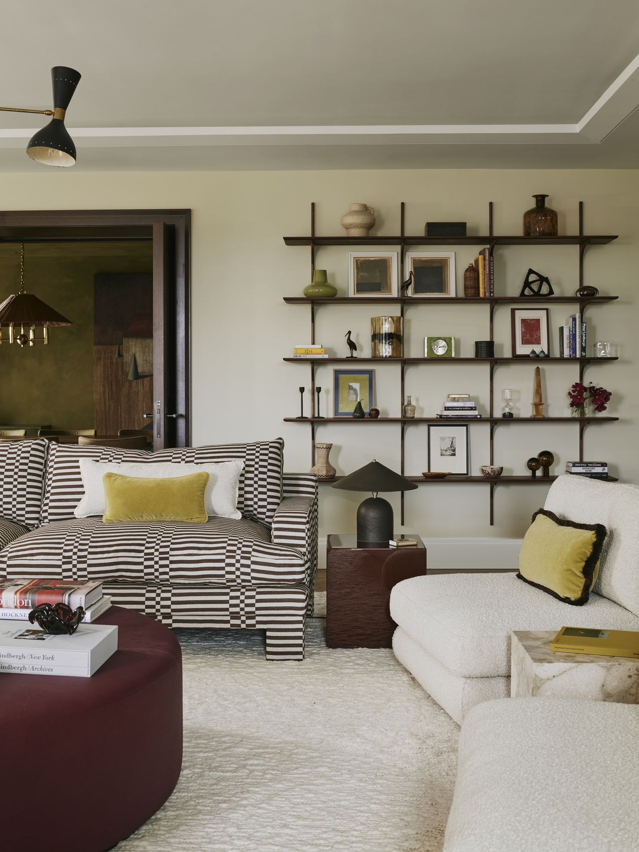 colorful living room with yellow sofa, striped sofas, boucle armchair, oxblood round ottoman coffee table, pendant light, and square side table with lamp