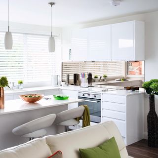 white kitchen with island and white leather bar stools with mirror splashback