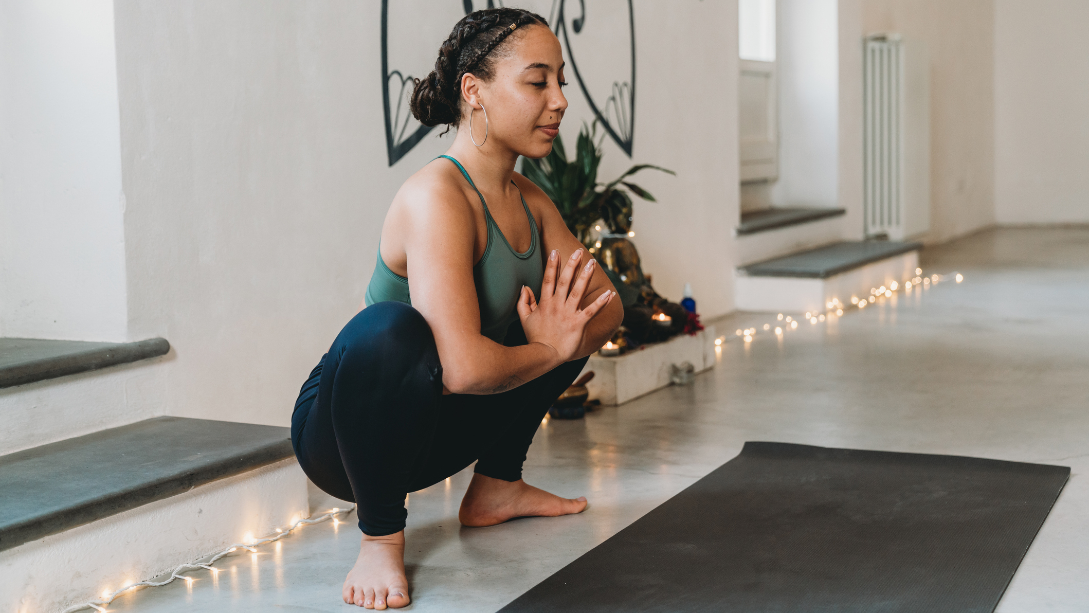 Woman sits in garland pose in a yoga studio