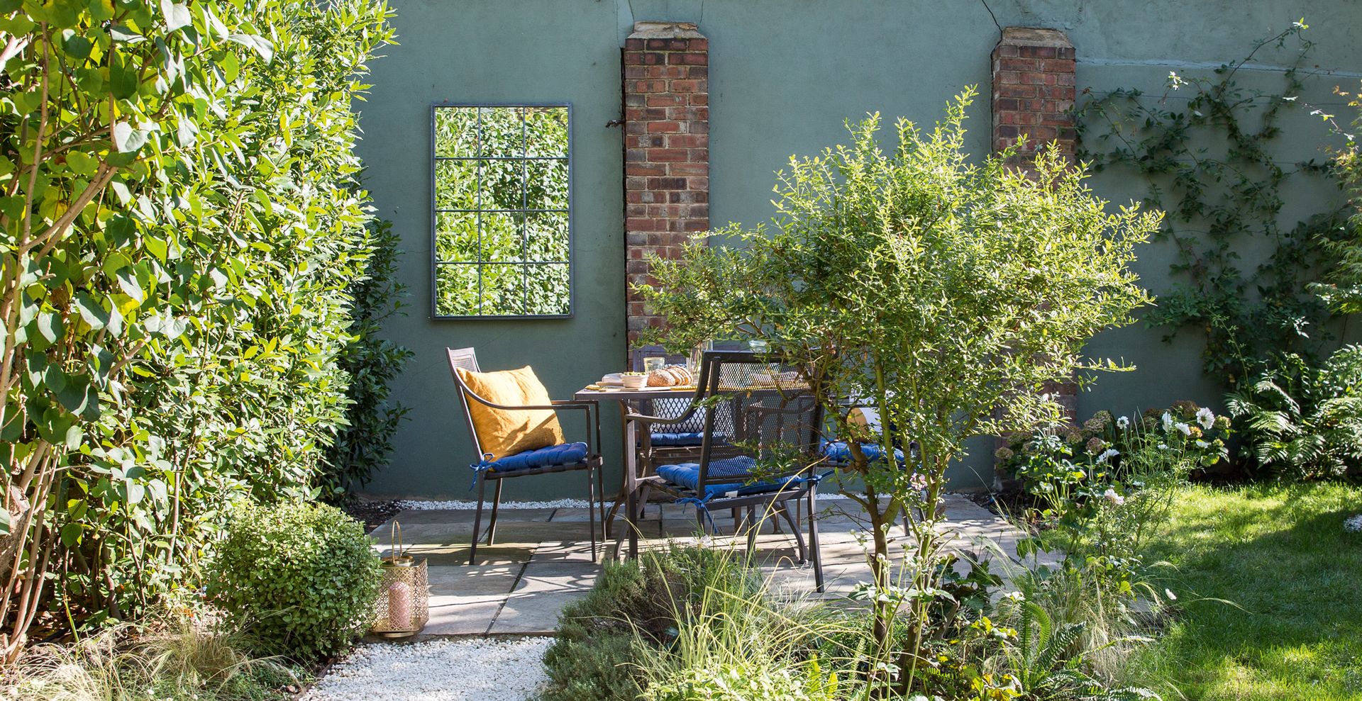 Small garden with green painted wall with garden mirror to show how to make a small garden look bigger