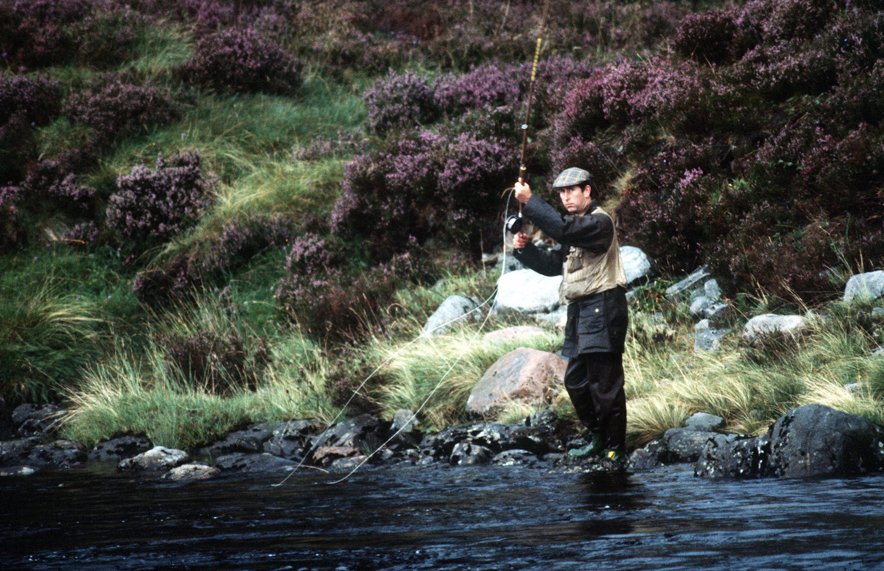 Prince Charles in fishing clothes casting on the banks of the River Dee