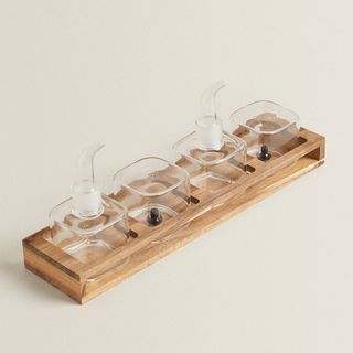 A slim wooden tray with two glass salad dressing bottles and two glass salt and pepper shakers, for Zara Home's summer sale.
