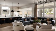 An open plan living room and kitchen space with a blue corner sofa, two curved accent chairs, and a neutral kitchen