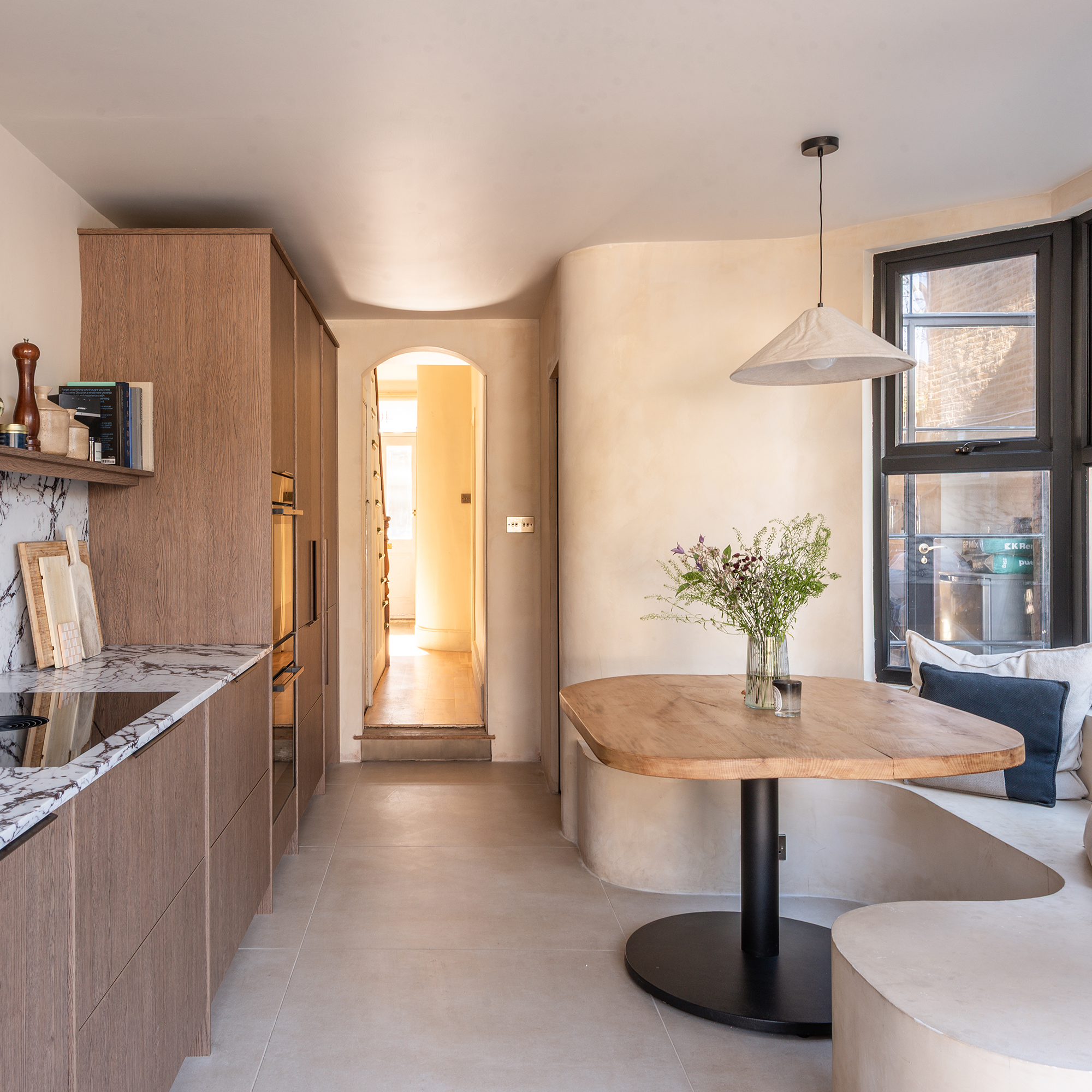 Off white kitchen with oak cabinets and a curved wall leading into a curved bench below a black-framed window