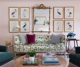 Pink living room with a gallery wall and an antique mirror that sits above a bench upholstered in green tropical print fabric.