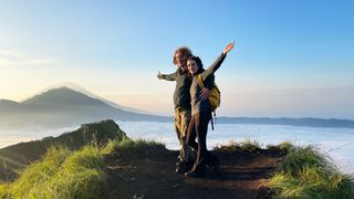 The author and partner on a mountain summit in bali at sunrise, with mountain shadows in the background and a blue morning sky