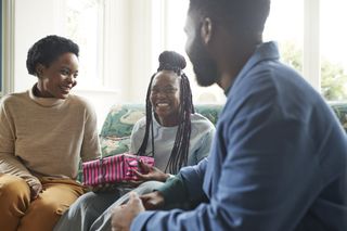 A mum, daughter and son sat on the sofa opening a present that has been regifted