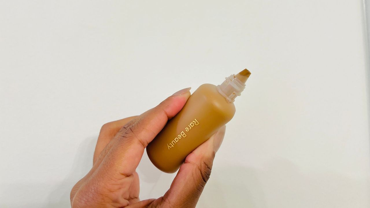 A person holding an opened Rare Beauty Tinted Moisturizer for the best foundations with SPF.