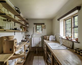 A utility room with wooden open shelving running the length of the room and a large farmhouse sink