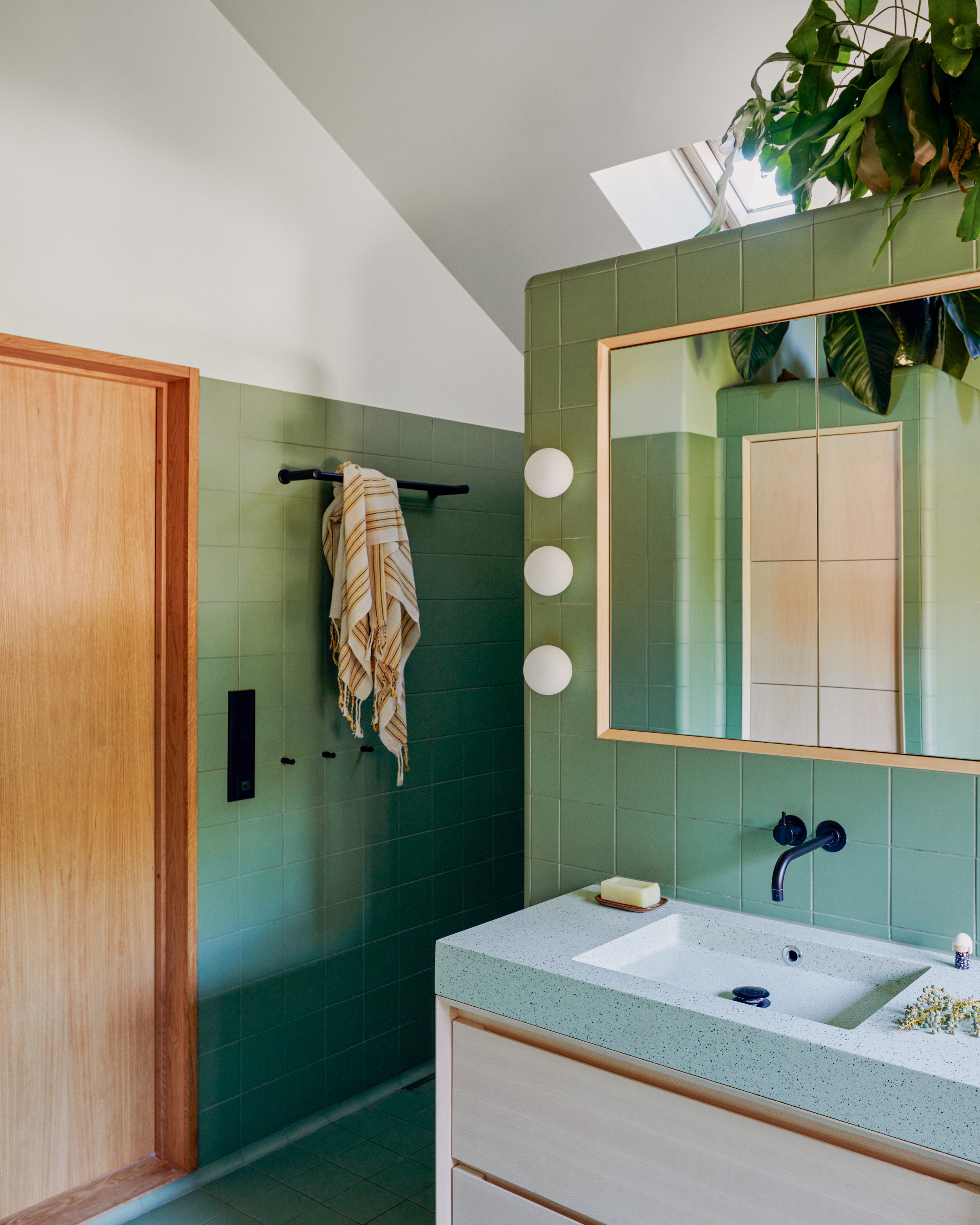 Bathroom with mint green tiles, wall-hung cabinet with mint terrazzo top, rectangular mirror and three globe wall lights