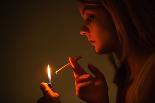 A woman lights a cigarette in a dark room