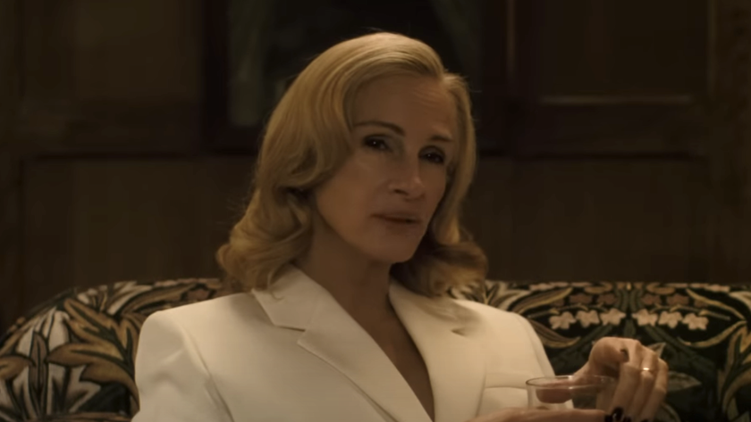 Julia Roberts sitting down in a white blazer and a drink in hand in After The Hunt