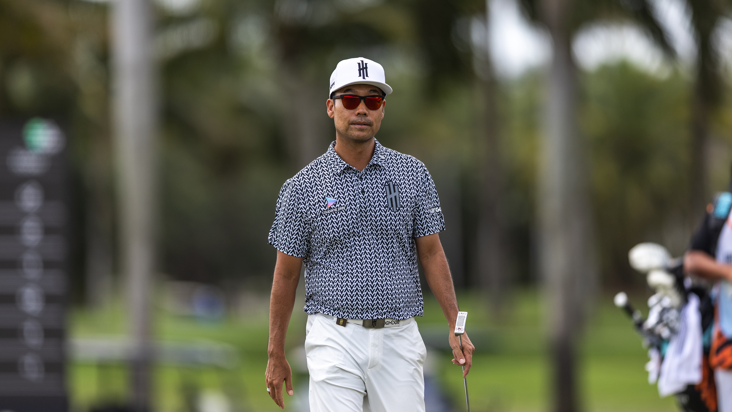 Kevin Na walks along holding his putter and wearing sunglasses during LIV Golf Miami 2025