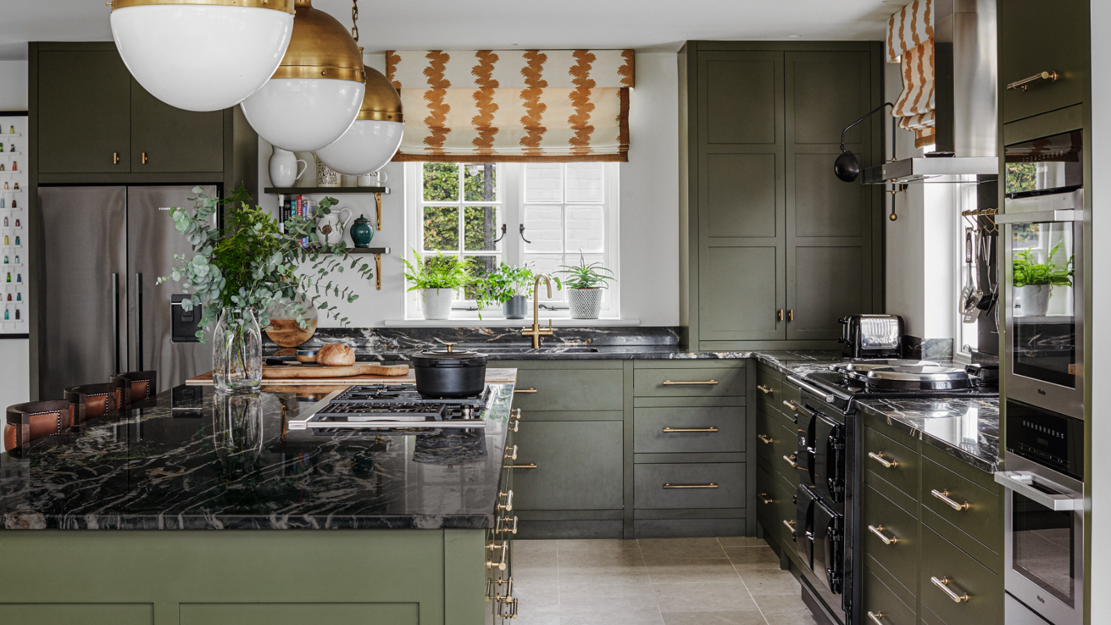 a green kitchen with black marble countertops and gold cabinet pulls