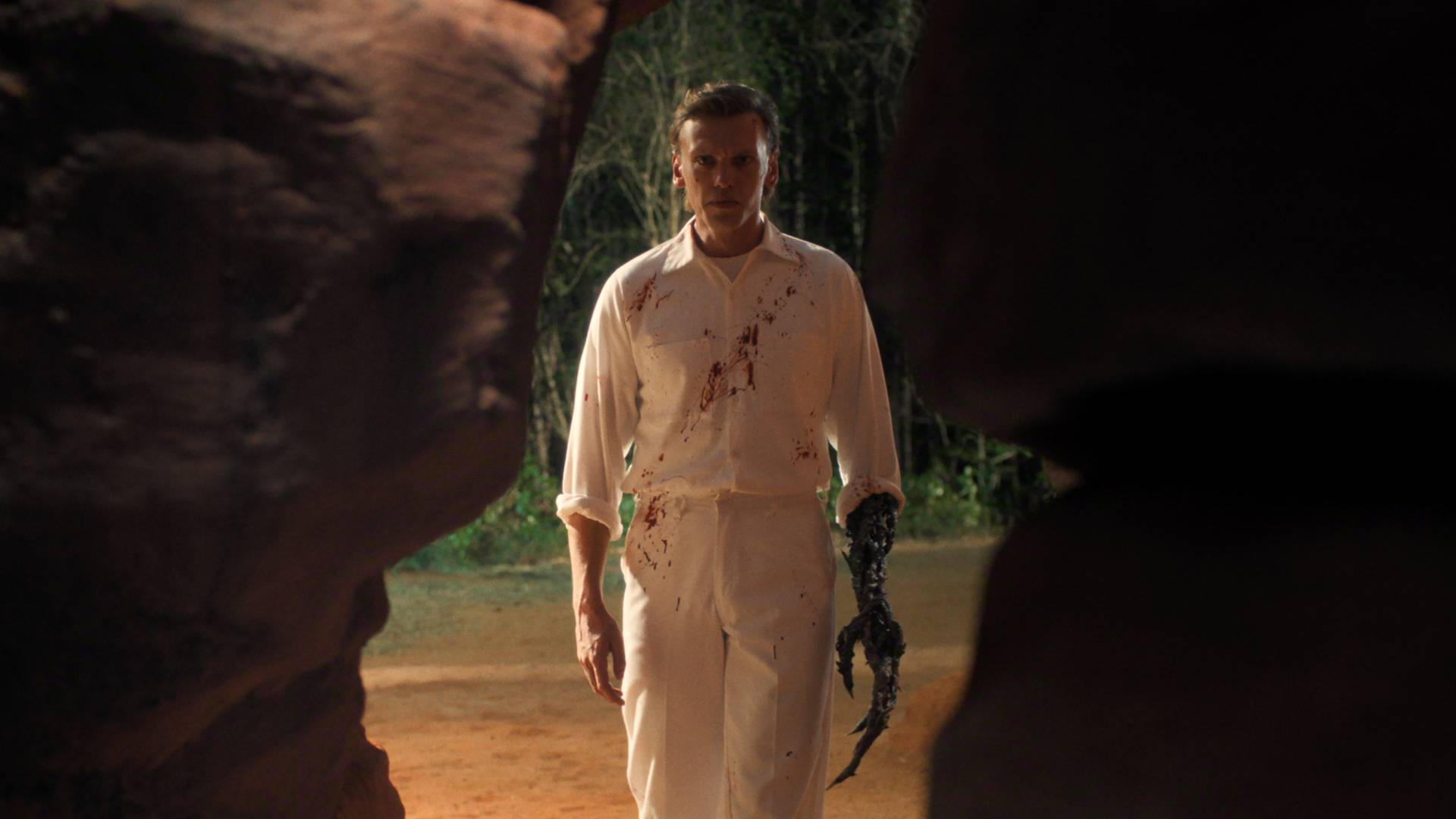 Jamie Cambell Bower as Henry Creel in Stranger Things season 5 volume 1, with a clawed hand and bloody shirt looking concerned as he stares into a cave