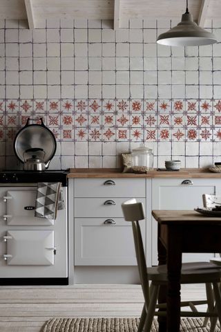 A rustic white kitchen with white aga range cooker and rustic white and terracotta patterned tile backsplash.