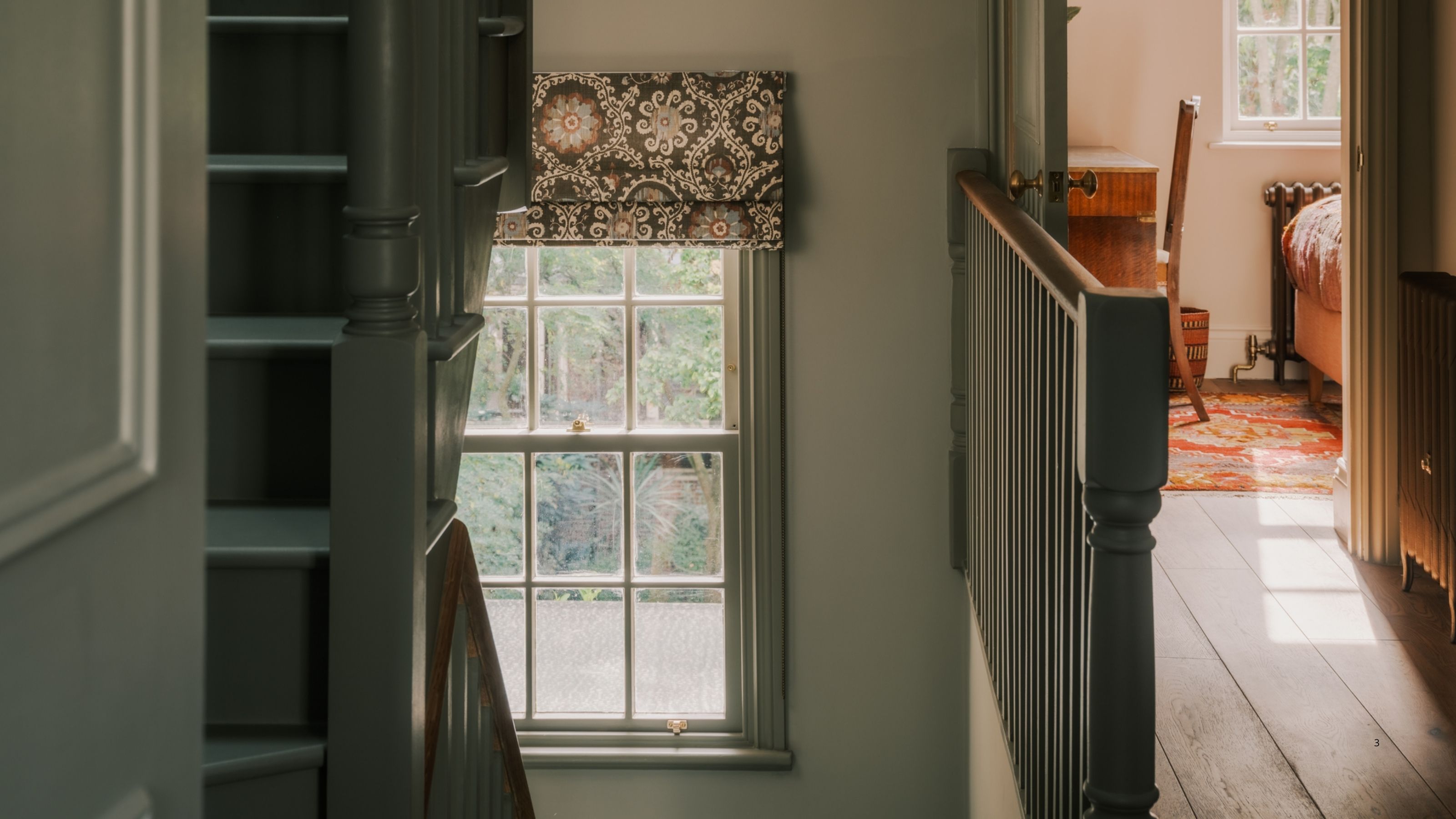 Image of a sage green stairwell with a window that has a patterned roman blind.