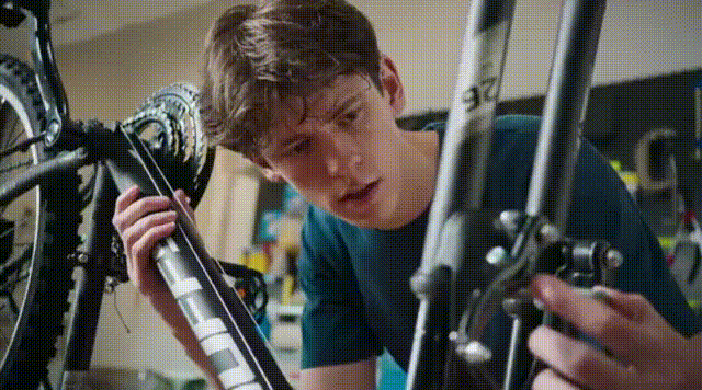 An animated GIF of a young man working on a bicycle and using Google AI on his phone.