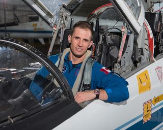 Canadian Space Agency astronaut Joshua Kutryk sits with his arm resting outside the cockpit of a jet. he wears a blue flight suit.