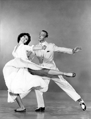 a promo shot for The band wagon of a woman in a white dress lifting her leg dancing with a man in a white suit