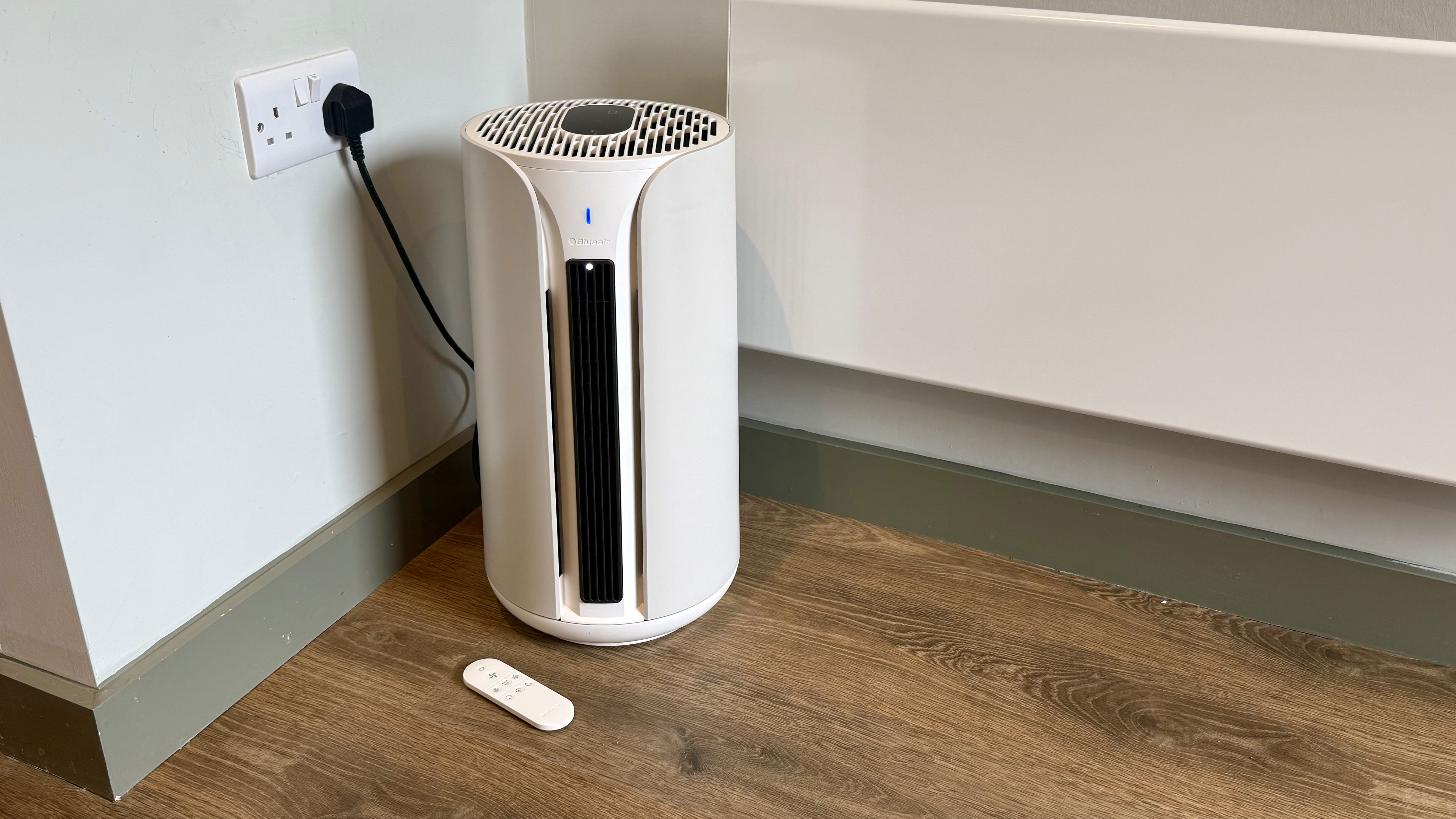 A photo of the Blueair T10i Air Purifier with its remote in a room with white walls and laminated wooden floors