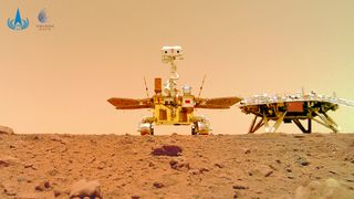 In a "selfie" taken on Mars, we see a rover standing next to its lander on the rocky red planet, with an orange sky in the background.