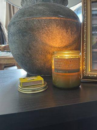 A lit soy wax candle in front of a stoneware lamp