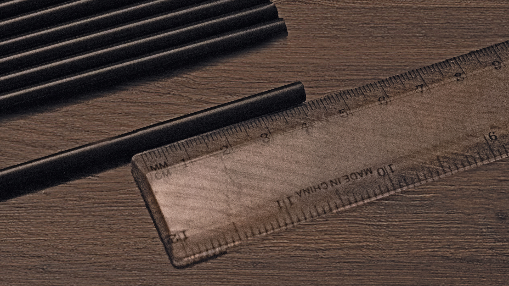 A close-up of black straws alongside a transparent ruler on a wooden surface, emphasizing measurement and school supplies