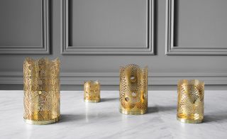 Four cylindrical, intricate gold candleholders