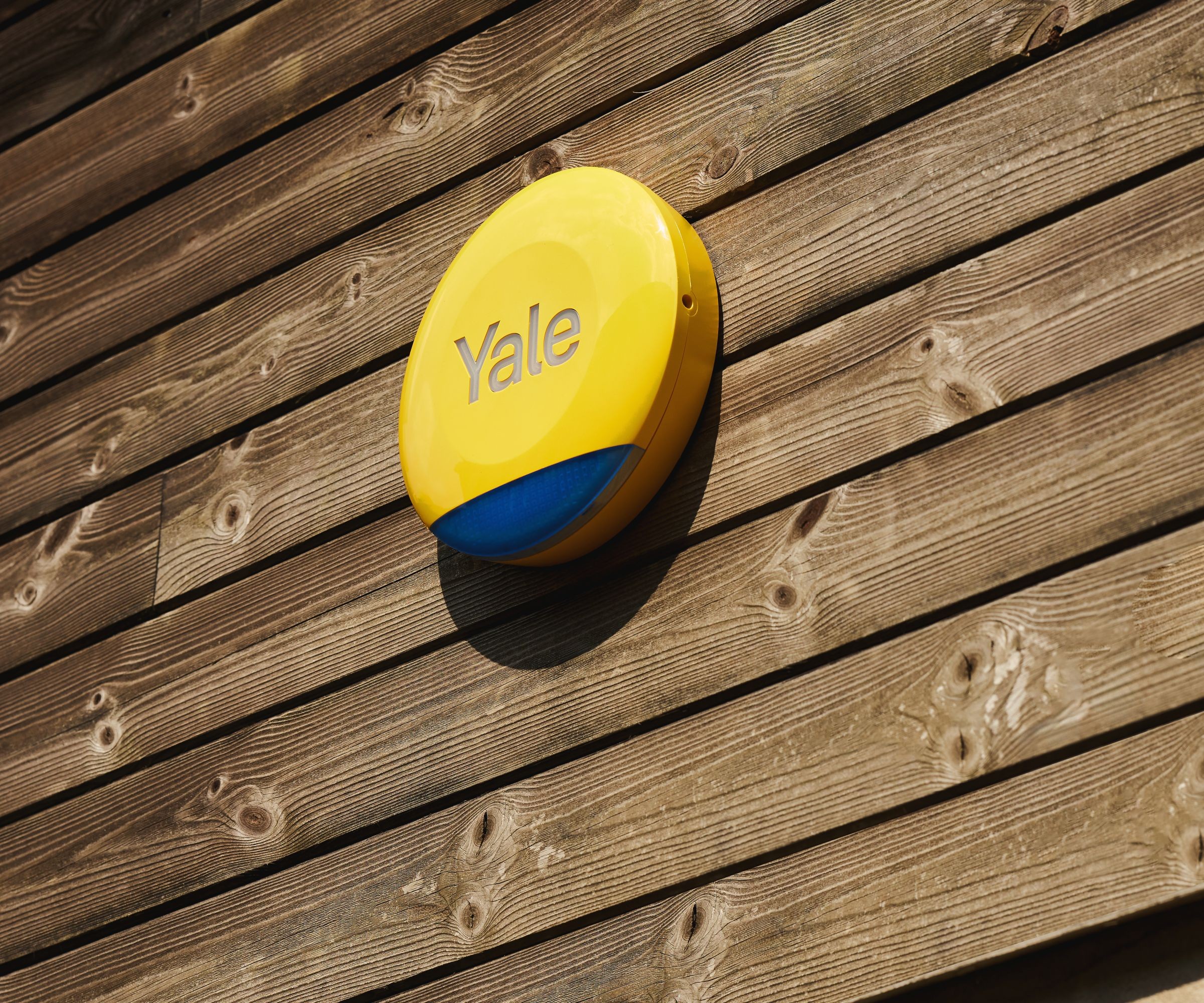 A close up of a yellow Yale alarm box on wooden cladding