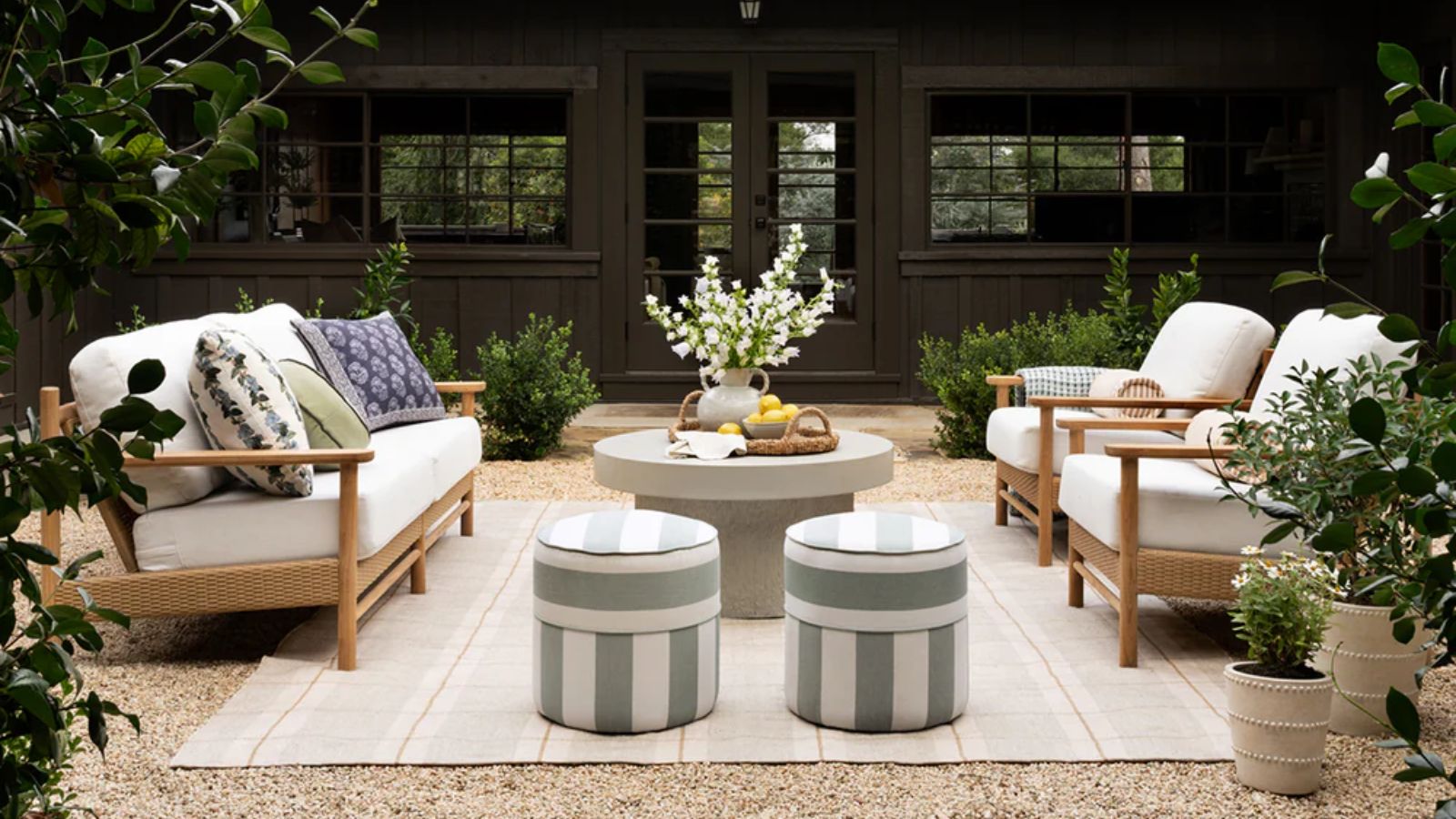 outdoor patio area on single styled with a large outdoor area rug, a concrete round coffee table, a wooden and neutral sofa with two matching armchairs and two small green striped ottomans