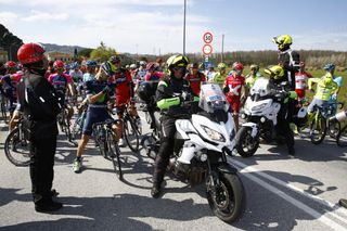 The peloton waits for the train to pass at the level crossing
