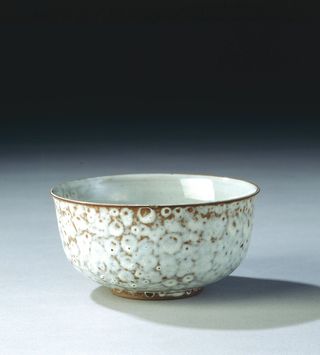 A white and gold ceramic bowl with textured detailing photograhed against an ombre (black to grey) background