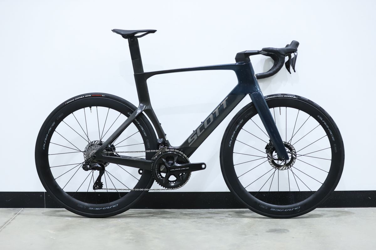 A blue Scott Foil RC Pro stands against a white wall