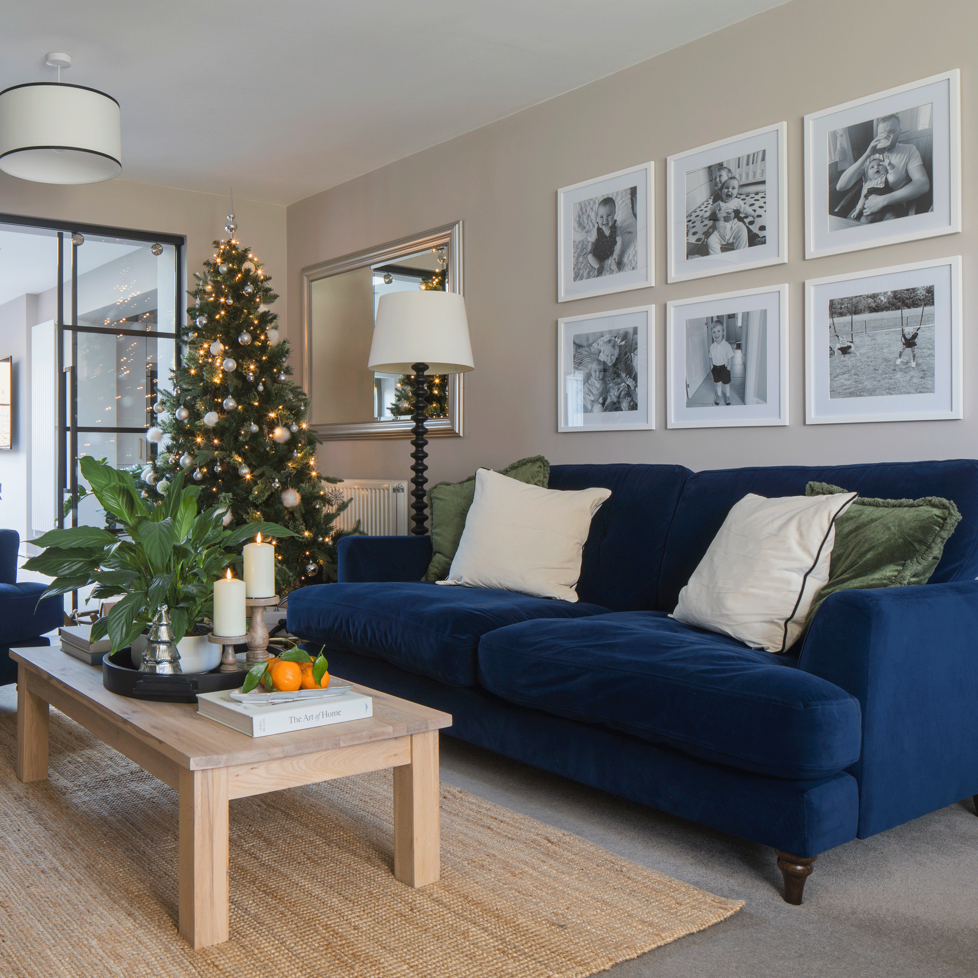 a living area with a blue sofa beside a Christmas tree with glass internal doors leading into a bright dining area